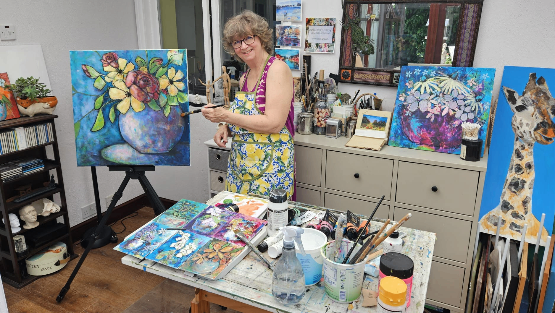 Leslie Robinson painting in her garden-room studio surrounded by floral works